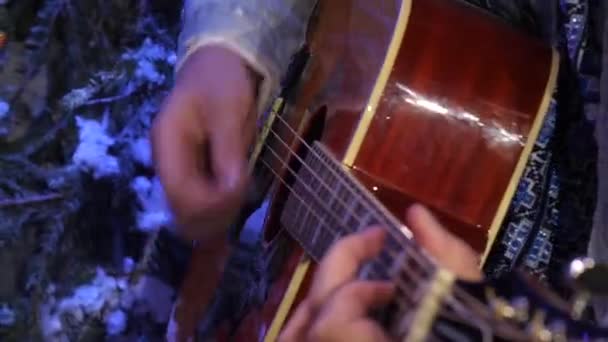 Un guitarrista de una chaqueta densa toca enérgicamente una púa sobre una guitarra acústica. - Imágenes, Vídeo
