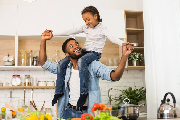 Cheerful black man holding his cute little daughter on shoulders - Foto, imagen