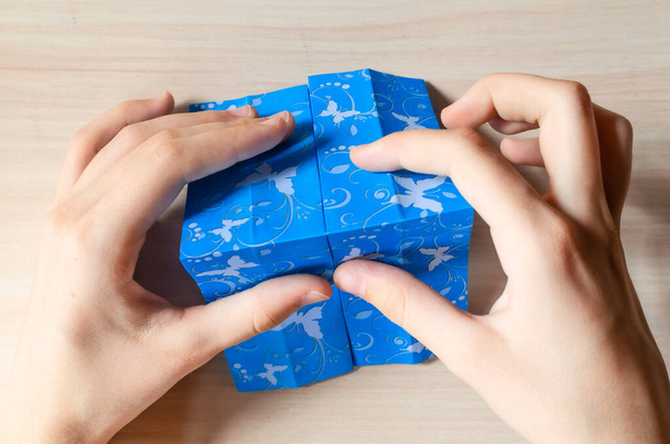 A lány kezei origami kék ruhát készítenek pillangó nyomtatott papírból. Lépésről lépésre, 9. lépés. Anyák napja, születésnap, nyári ajándék, családi szabadidő koncepció. DIY bemutató, lapos, felülnézet. - Fotó, kép