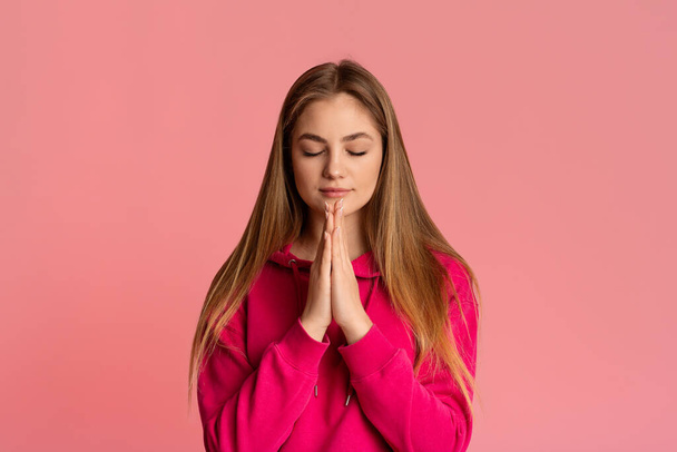 Η έφηβη προσεύχεται, σφίγγει τα χέρια και κλείνει τα μάτια. - Φωτογραφία, εικόνα
