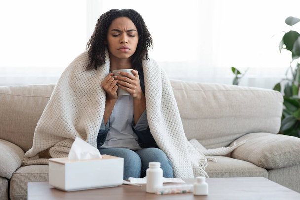 Chorą czarną kobietę czującą się źle w domu, pijącą herbatę na kanapie - Zdjęcie, obraz