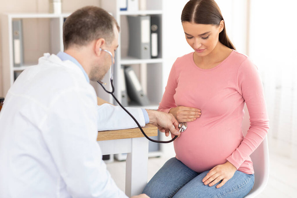 Зріла досвідчена лікар оглядає молоду вагітну жінку
 - Фото, зображення