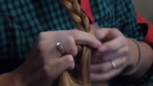Caucasian woman in a green plaid shirt combing her hair in a braid - Footage, Video