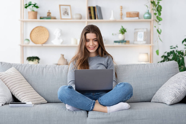 Chica positiva en busca de trabajo en línea desde casa, utilizando el ordenador portátil
 - Foto, Imagen