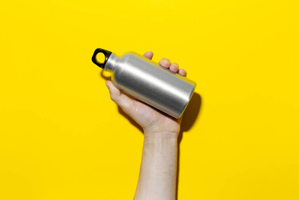Close-up of male hand holding reusable aluminum thermo water bottle on background of yellow color. - 写真・画像