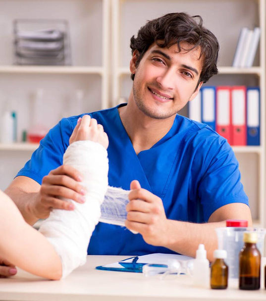 Junge Frau mit bandagiertem Arm besucht männlichen Arzt - Foto, Bild