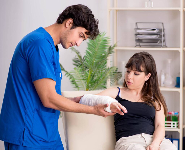 Junge Frau mit bandagiertem Arm besucht männlichen Arzt - Foto, Bild
