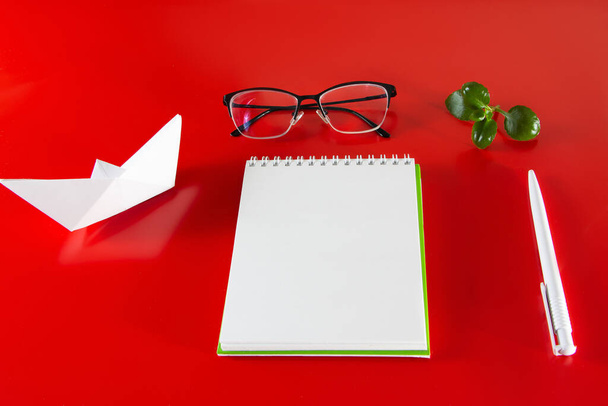 Material de oficina sobre fondo rojo. Cuaderno en blanco, bolígrafo y gafas. Diseño para el diseño en el estilo del minimalismo. - Foto, Imagen