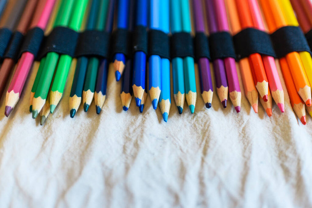 Φωτεινά χρωματιστά μολύβια σε μια μολυβοθήκη. Καφέ, ροζ, πράσινο, μπλε, γαλάζιο, βιολετί, πορτοκαλί, κόκκινο, κίτρινο. Σχολικές προμήθειες για παιδιά. Μπεζ χώρος αντιγραφής. - Φωτογραφία, εικόνα