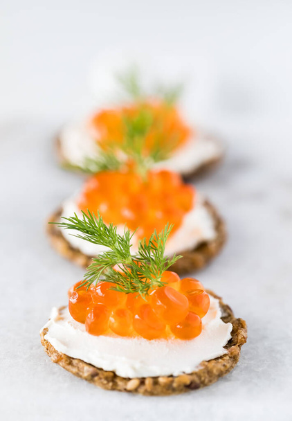 Un primer plano de una fila de galletas rústicas de grano entero rematadas con queso crema y caviar y decoradas con eneldo
. - Foto, imagen