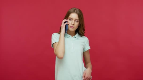 Pleasant conversation on mobile phone, cellular and roaming. Young beautiful woman in polo t-shirt talking on cellphone and smiling, chatting with friend. indoor studio shot isolated on red background - 映像、動画