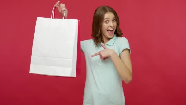 Happy shopper, store customer, young woman in polo t-shirt raising shopping bags with white empty copy space, pointing at packages and smiling, satisfied with purchase. indoor studio shot isolated - Filmati, video