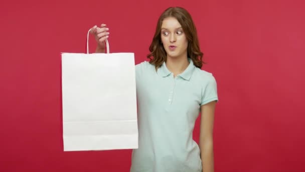 Amazed shopper, store customer woman in polo t-shirt looking inside shopping bags with white empty copy space, pointing at packages and expressing surprise, shocked by purchase. studio shot isolated - Metraje, vídeo