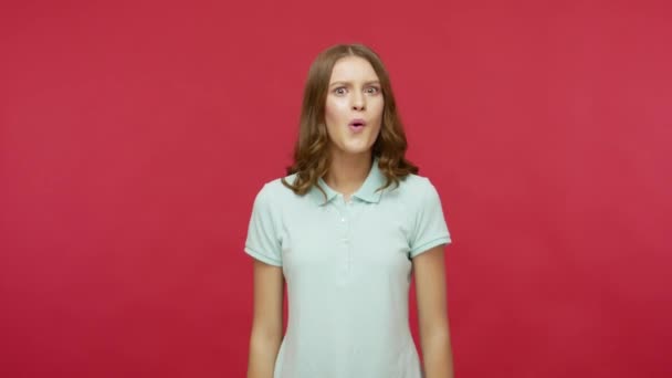Surprised young brunette woman in polo t-shirt emotionally reacting to sudden victory, shouting Wow, expressing disbelief in success, amazed and shocked by win. studio shot isolated on red background - Кадры, видео