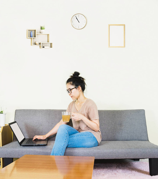 Young beautiful asian woman wore brown t shirt and jean, lying and sitting on gray sofa ,work online lifestyle,relax at home with coffee mug,home working laptop,work from home - Fotó, kép