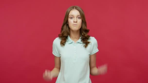 Enraged angry brunette woman in polo t-shirt clenching teeth and raising fists, looking at camera with irritated aggressive grimace, expressing furious emotions. studio shot isolated on red background - Video