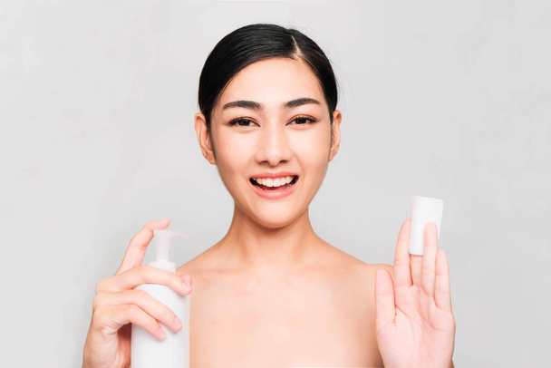 Temiz ve parlak ciltli genç Asyalı kadın, Kozmetik Güzellik Konsepti, yanağına dokunan eller, gri arka planda izole edilmiş gülen ve arkadaş canlısı yüz. - Fotoğraf, Görsel