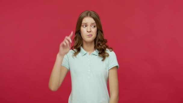Silly idea! Upset frustrated woman in polo t-shirt making stupid gesture with finger near head, dumb insane mind, looking with displeased unhappy expression. studio shot isolated on red background - Imágenes, Vídeo