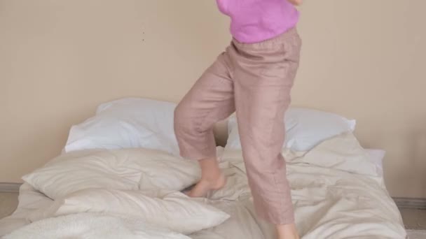 The girl dances on the bed, falls on the pillows and plays. Side view - Filmagem, Vídeo