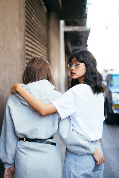 En iyi arkadaş kızlar sokakta yürürken, kollarını birbirlerinin boynuna dolayıp, biri arkasına dönüp kameraya bakıyordu.. - Fotoğraf, Görsel