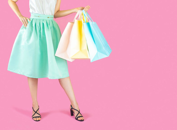 The female body part wore blue skirt and black High heels. Carrying a shopping bag in many pastel colors on pink background selective focus,shopping concept - Foto, Imagem