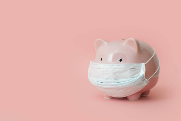 Close-up of pink piggy bank with medical mask is standing on pale pink background. Concept of frozen bank accounts and deposits and reserve accumulation for hard times. advertising space - Fotó, kép