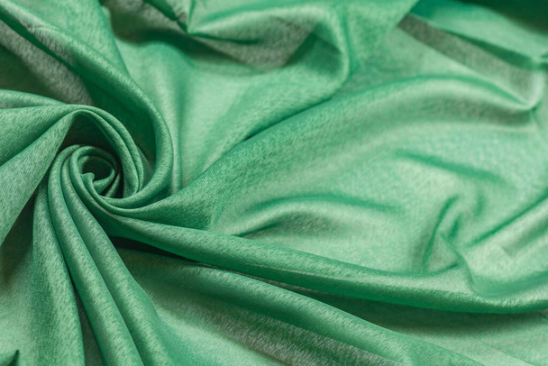 Geknitterte grüne gebogene Stofffragment mit Wirbel als Stoff Hintergrund Textur - Foto, Bild