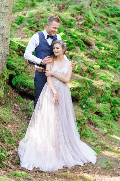 Ένα ελκυστικό νιόπαντρο ζευγάρι, μια ευτυχισμένη και χαρούμενη στιγμή. Ένας άντρας και μια γυναίκα ξυρίζονται και φιλιούνται με ρούχα διακοπών. Βοημίας-style γαμήλια cermonia στο δάσος στον καθαρό αέρα. - Φωτογραφία, εικόνα