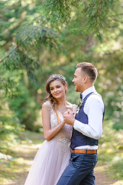 Egy vonzó friss házaspár, egy boldog és örömteli pillanat. Egy férfi és egy nő borotválkozik és csókol ünnepi ruhában. Bohém stílusú esküvői cermónia az erdőben a friss levegőn. - Fotó, kép