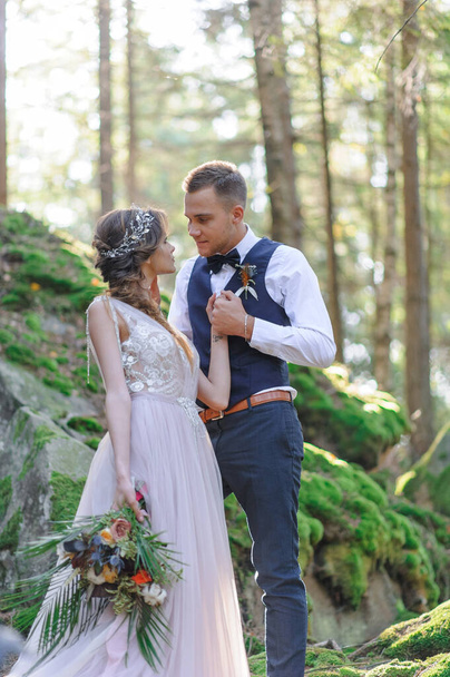 魅力的な新婚カップル、幸せと喜びの瞬間。休日の服装で男と女が剃りキス。新鮮な空気の森の中でボヘミアンスタイルの結婚式のセルモニア. - 写真・画像