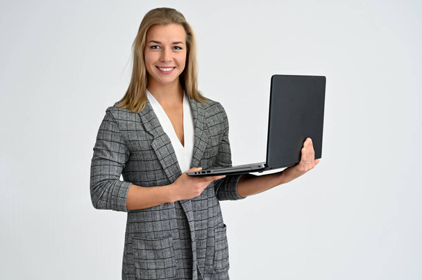 Close-up portrait of a cute caucasian blonde female student girl in a gray jacket on a white background with a laptop. Wide smile, happiness. It is in different poses. - Foto, immagini