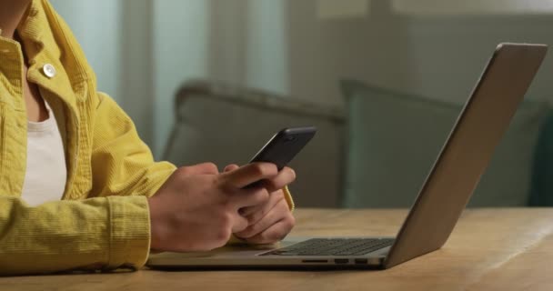 Mid section close up of a Caucasian woman spending time at home, social distancing and self isolation in quarantine lockdown, sitting at a table, using a smartphone and a laptop - Filmagem, Vídeo