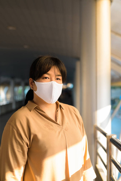 Retrato de mulher asiática com sobrepeso com máscara para proteção contra o surto do vírus da corona na ponte do skywalk na cidade - Foto, Imagem