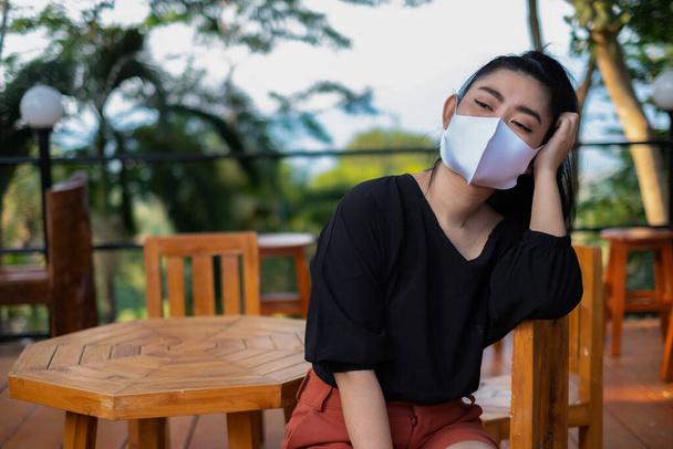 Молодая женщина Азии сидит на стуле дерева и надеть маску для защиты от респираторных заболеваний в воздухе, как грипп пыли и смога в парке, женщин концепции вируса безопасности инфекции
 - Фото, изображение