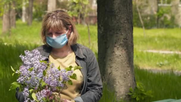 Nuori nainen lääketieteellisessä naamiossa kukkakimpun kanssa. Käsite terveys ja turvallisuus, COVID 19 sepelvaltimovirus karanteeni, virussuojelu
 - Materiaali, video
