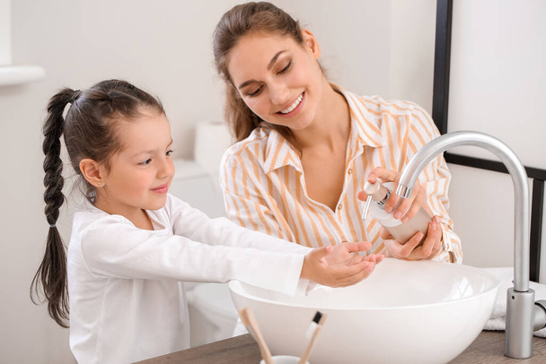 Little daughter with her mother washing hands in bathroom - Fotó, kép