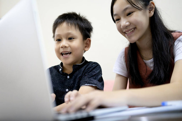 Αδέρφια αγόρι και το κορίτσι παιδί απολαμβάνουν να παίζουν online παιχνίδι στον υπολογιστή laptop, ασιατική αδελφή, ο μικρός αδελφός έχει τη διασκέδαση βλέποντας σε απευθείας σύνδεση κινούμενα σχέδια μαζί, μείνετε στο σπίτι, εθισμός στα μέσα κοινωνικής δικτύωσης στο διαδίκτυο - Φωτογραφία, εικόνα