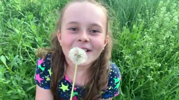 Blondes Mädchen bläst Löwenzahn in den grünen Garten - Filmmaterial, Video