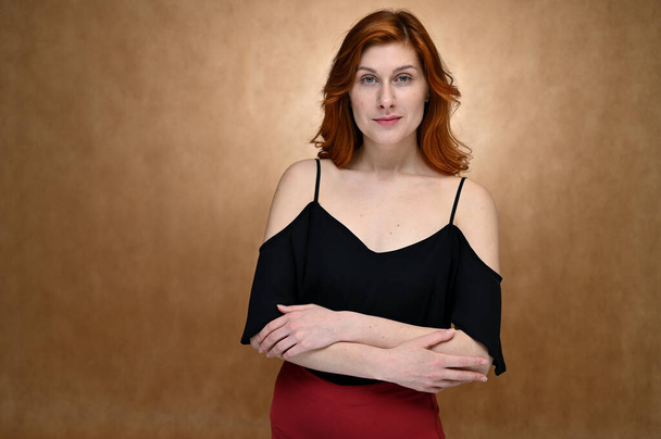 Portrait of a pretty red-haired young woman in a black blouse. Model posing in the studio on a beige background. - Photo, Image