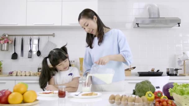 Boldog ázsiai család, hogy a reggelit a konyhában otthon. Az anya, aki tejet önt az üvegbe, reggel adja a lányát. Családi főzés koncepció. Lassú mozgás. - Felvétel, videó