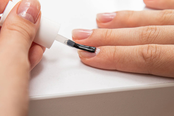 Das Mädchen lackiert ihre Nägel mit Nagellack auf den Händen mit einem Pinsel in Nahaufnahme. - Foto, Bild