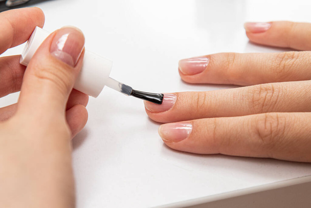 Het meisje verft haar nagels met nagel Pools op haar handen met een borstel close-up. - Foto, afbeelding