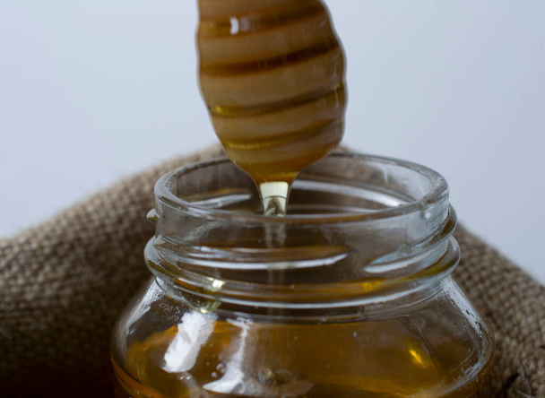 selective focus. honey flows from Honey Dipper, into a jar of honey. jar in a sackcloth bag. healthy life concept. close-up - Foto, imagen