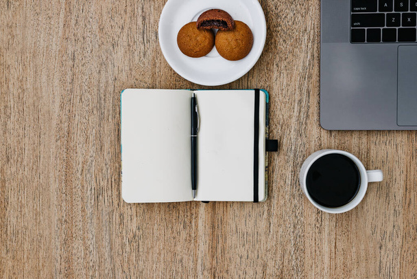 Flat lay of the workplace. Freelance work laptop smartphone and note pad. Morning coffee with cookies. Copy space on wooden background and notepad. Top view, a notebook next to a laptop, a pen for recording cases. Place for text - Foto, Bild