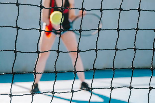 A young woman playing tennis on the other side of the tennis net - Foto, Imagen