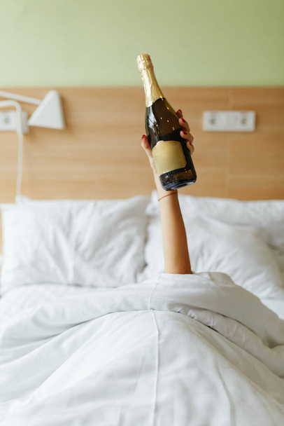 Руки жінки з пляшкою і склянкою шампанського в ліжку
 - Фото, зображення