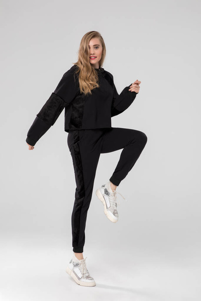 cute blonde girl posing in chic long sleeve black sports wear. white sneakers. white background. - Photo, Image