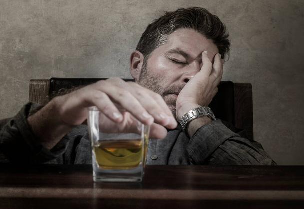 young messy and drunk alcohol addict man drinking whiskey glass at home sitting thoughtful and depressed as alcoholic suffering alcoholism problem and addiction intoxicated and lost - Foto, afbeelding