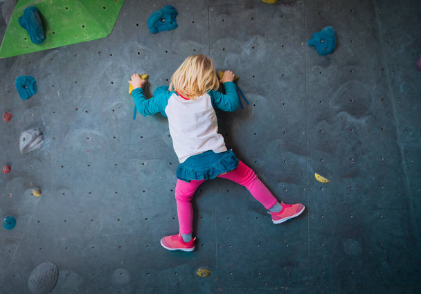 Mała dziewczynka wspina się na sztuczne głazy ściany w siłowni - Zdjęcie, obraz
