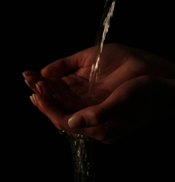 A stream of water flows in the palm of the hand. Low key photography. Focus on the foreground. - Фото, изображение